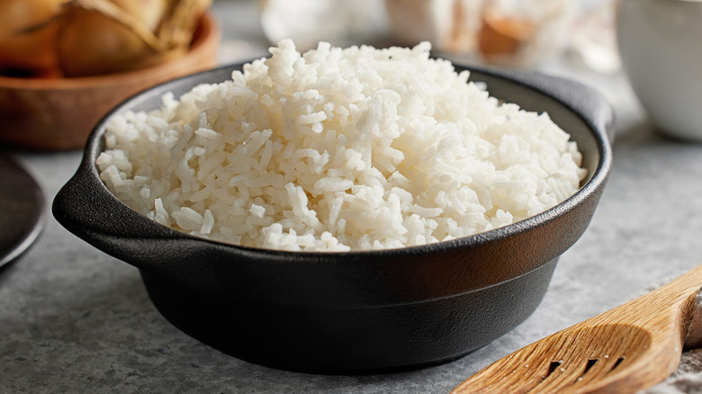 Bowl of fluffy white rice sitting on a table with a serving spoon by its side.