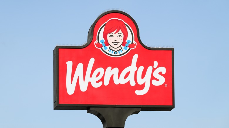 A big Wendy's sign with its logo, set against a clear blue sky