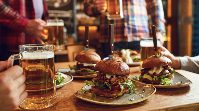 People's hands holding beers around a table filled with burgers