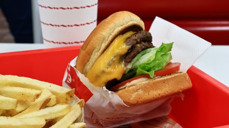 An In-N-Out cheeseburger in its wrapper next to fries and a drink on a tray