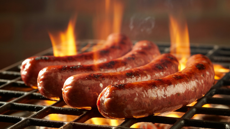 Four sausages grilling over a bed of flames