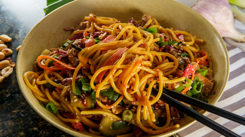 A bowl of spicy Thai peanut butter lo mein noodles with sesame seeds.