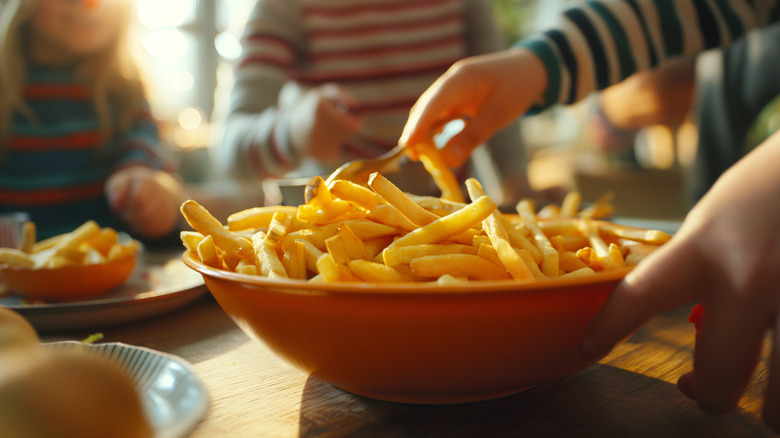 Hands reach into a bowl of french fries