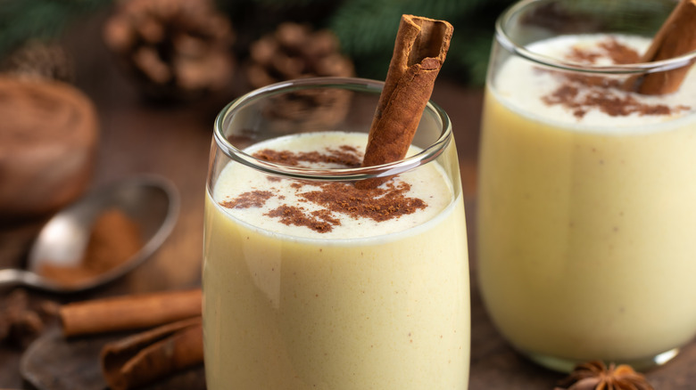 Two glasses of eggnog are garnished with cinnamon sticks.