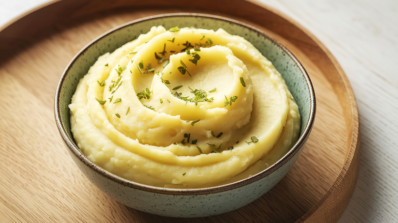 Mashed potatoes garnished with parsley sitting on a wooden tray