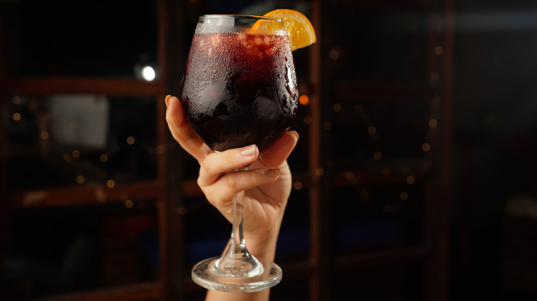 Hand holding glass of red sangria with orange slice garnish