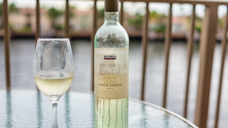 A bottle of Kirkland pinot grigio wine on a table next to a glass with wine in it.