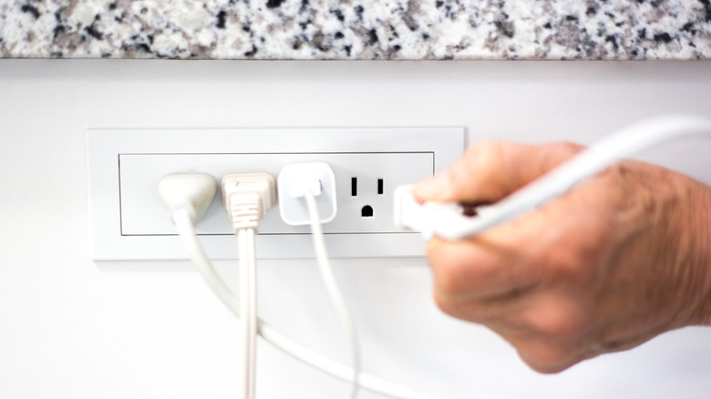 A hand plugging something into an electrical outlet