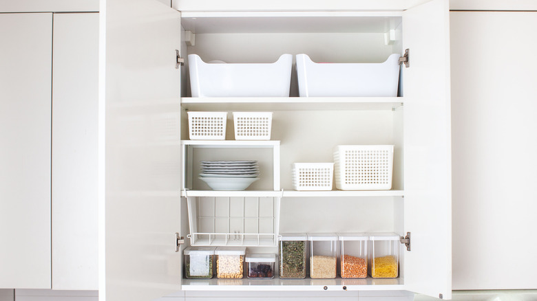 An open kitchen cabinet with plates, jars, and baskets