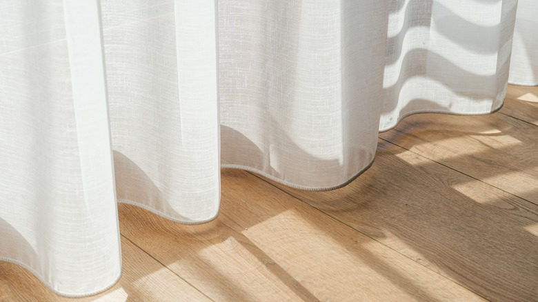 The hem of the curtains, with light sipping through and spilling onto the hardwood floors