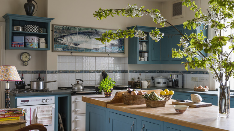 A cozy, character-filed kitchen with blue-green cabinets, charming art and trinkets, playful accents, and a statement plant