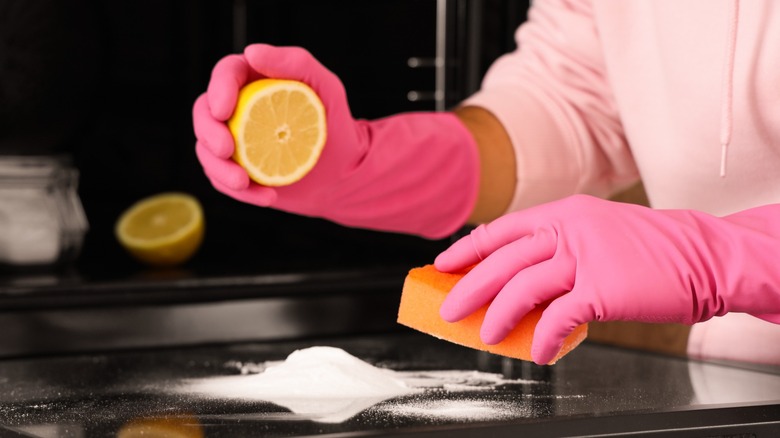 Hands in pink gloves cleaning a surface with a sponge and half lemon