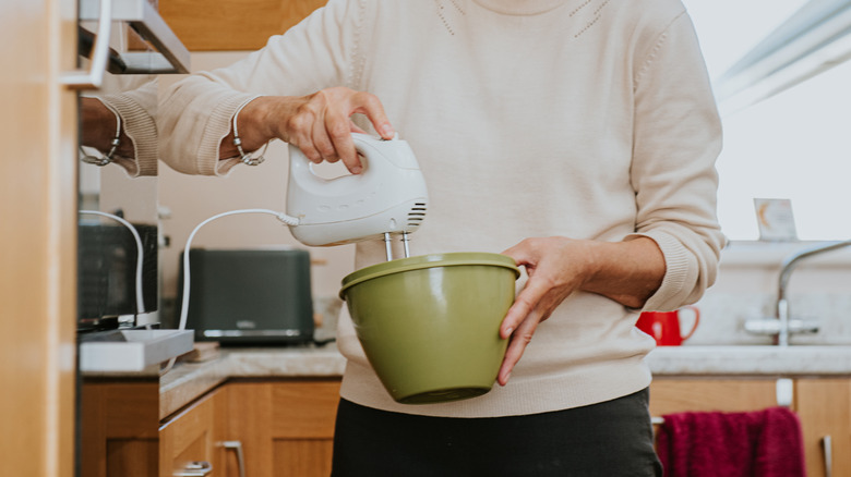 A person using an electric beater to mix ingredients in a bowl