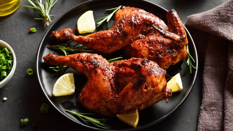 Crispy chicken halves on a platter garnished with herbs and citrus