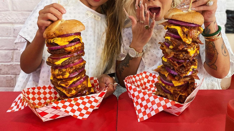 Two people holding up Heart Attack Grill's octuple bybass burgers