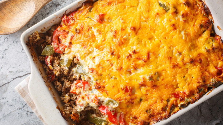 A mouthwatering casserole dish topped with melted cheese, partly scooped out to reveal meaty layers