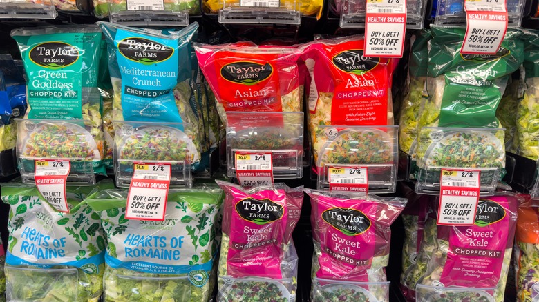 A grocery store refrigerator case full of a variety of bagged salads.