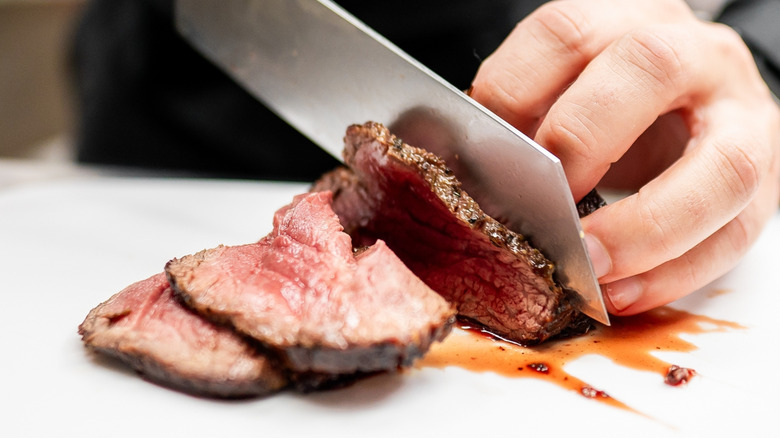 Close up of hand slicing steak with large knife.