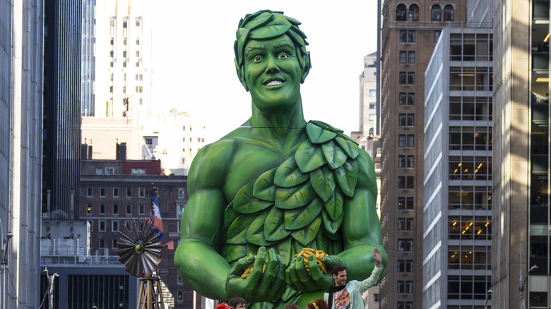 A huge parade float of the Jolly Green Giant, who is holding green beans in his hands