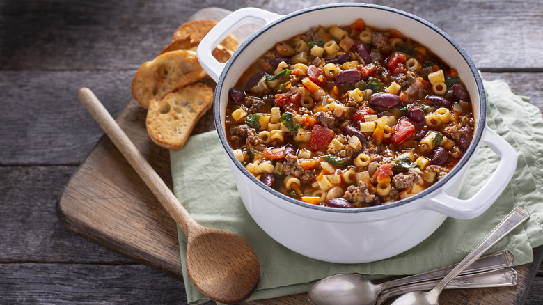 close-up of pasta fagioli on a green cloth next to toasted bread and a spoon