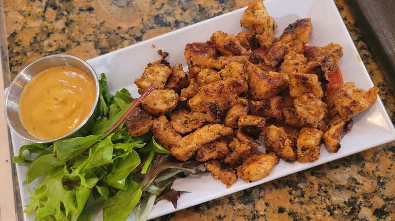 A plate with blackened (spice-rubbed, seared) alligator and dipping sauce