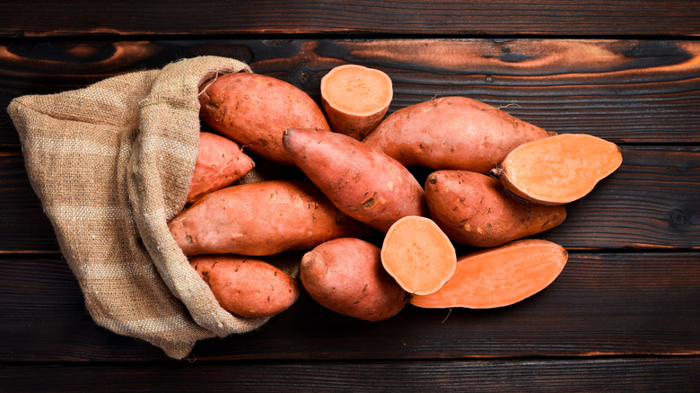 Raw sweet potatoes spilling out of burlap bag on a wooden table