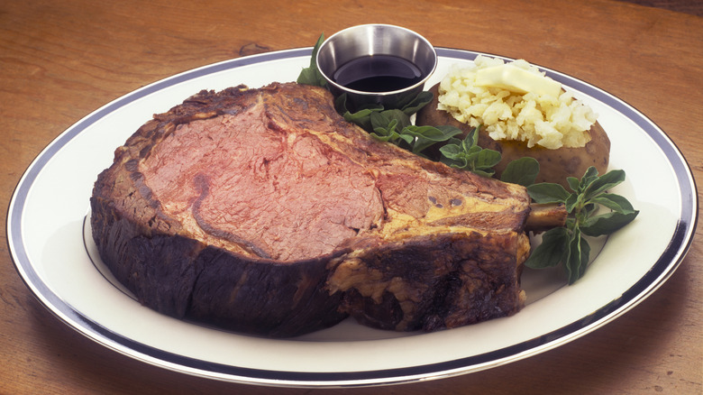 Roasted prime rib sitting on a plate with a baked potato