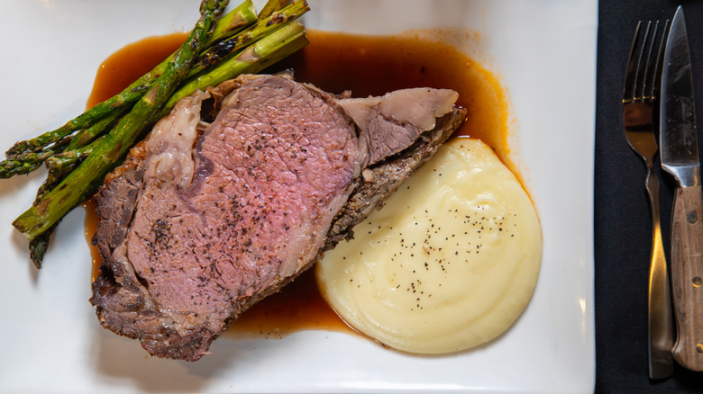 A medium roasted prime rib plated with asparagus and mashed potatoes