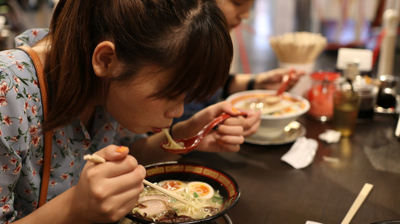 A woman eating ramen from a spoon at a restaurant
