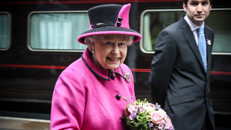 Queen Elizabeth II smiles in pink while holding fresh flowers