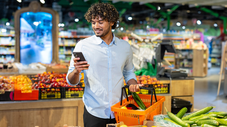 A man browsing his smartphone while grocery shopping.