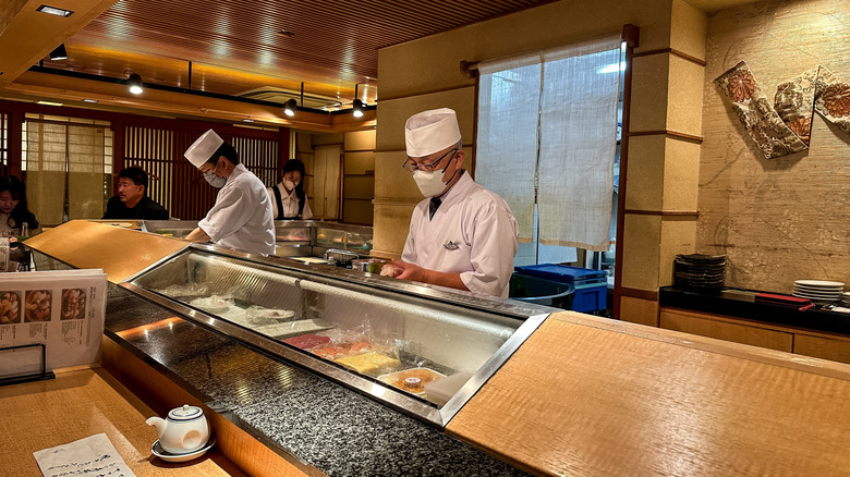 A typical sushi restaurant where fish is displayed on glass by the bar, while a sushi chef stands behind the counter