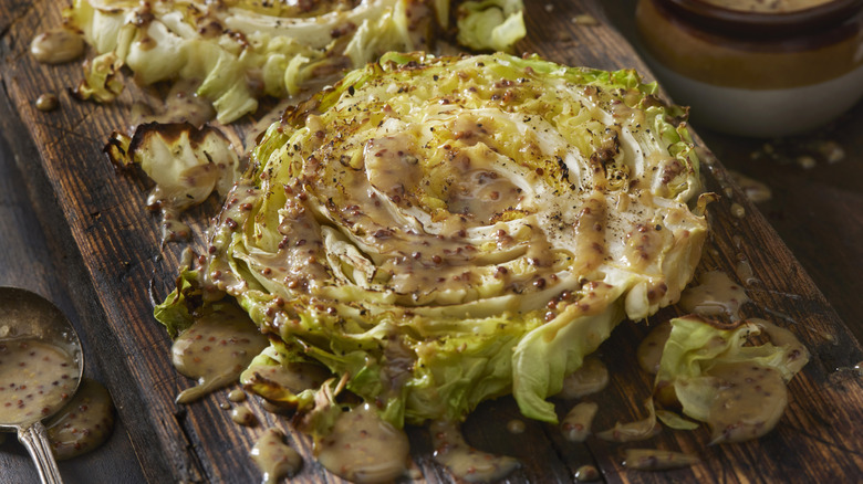 Half head of roasted cabbage on wood cutting board with vinaigrette