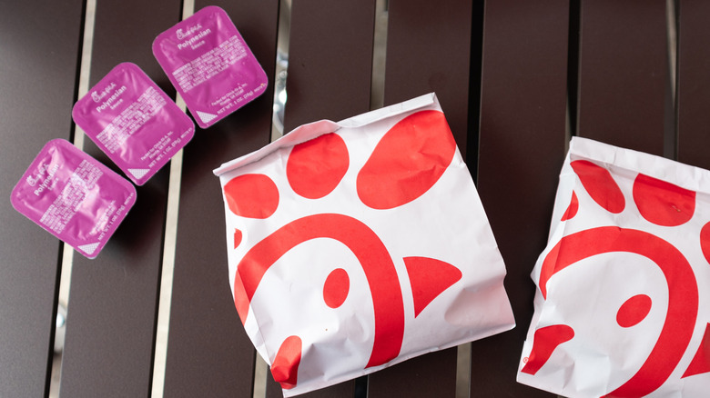 Three packets of Chick-fil-A Polynesian Sauce sit on a table alongside two Chick-fil-A bags.
