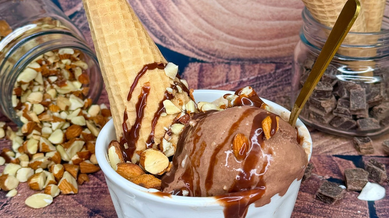 A scoop of chocolate ice cream with almonds in a cup with a spoon and waffle cone