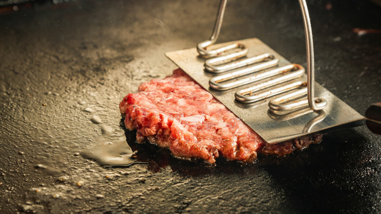 A smash burger being pressed onto a grill.