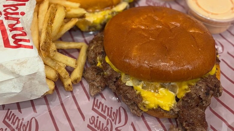 A Skinny Louie smash burger next to some fries on greaseproof paper.