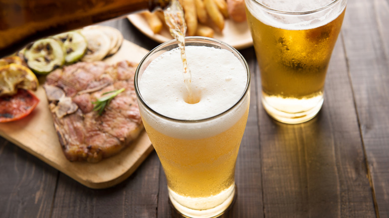 Bottle pouring beer into a cup next to plates of steak and fries