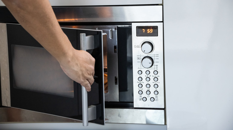 A hand opening a microwave door