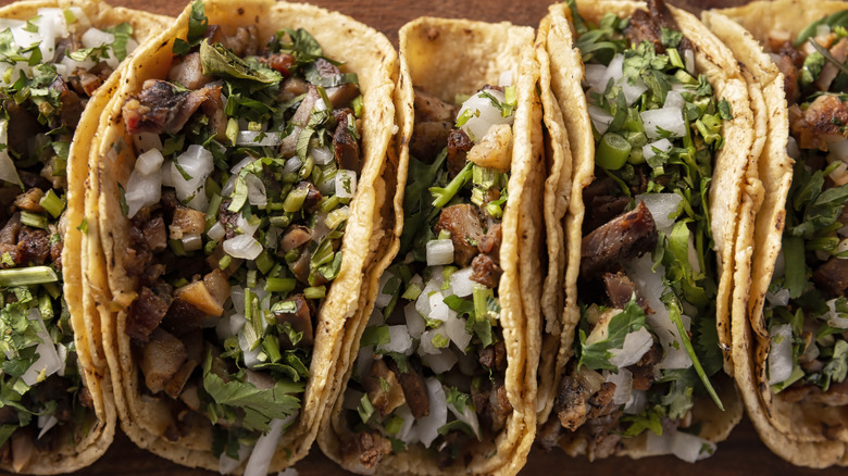 A couple of tacos stacked neatly beside each other, all loaded with veggie and meaty ingredients