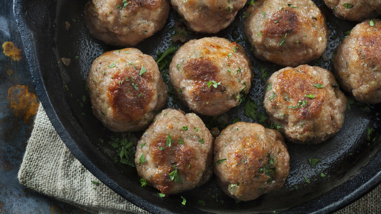 Several meatballs in a cast-iron pan.