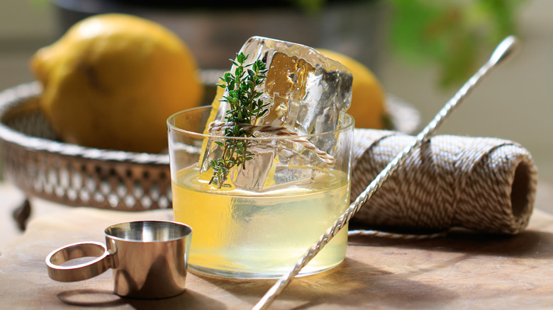 A white Negroni in a rocks glass with a large ice cube in a pleasant outdoor setting