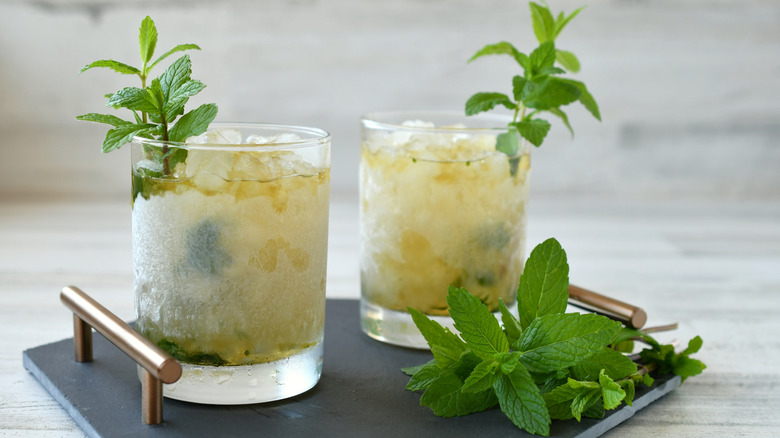 Two mint juleps in a clear whiskey glasses with mint