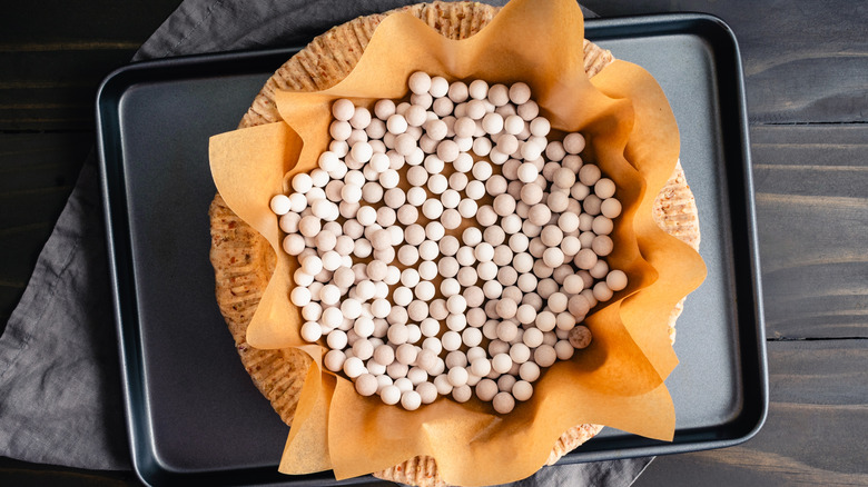 Raw pie crust with pie weights on a nonstick baking sheet.
