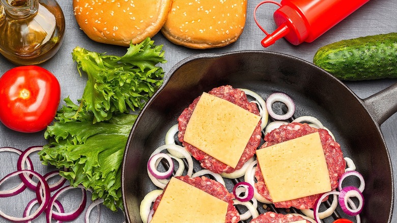 Raw beef patties with cheese in a cast iron pan with sliced raw onions