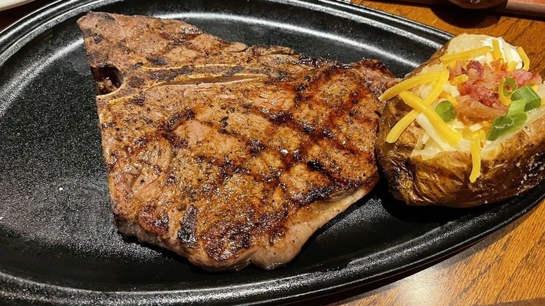 Outback Steakhouse's Melbourne Porterhouse served on a black plate with a loaded baked potato