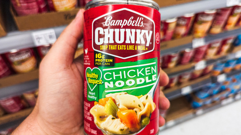Someone holds a can of Campbell's Chunky Chicken Noodle Soup inside a grocery store