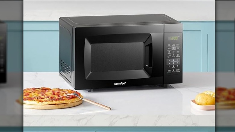 Comfee microwave sitting on a counter next to pizza
