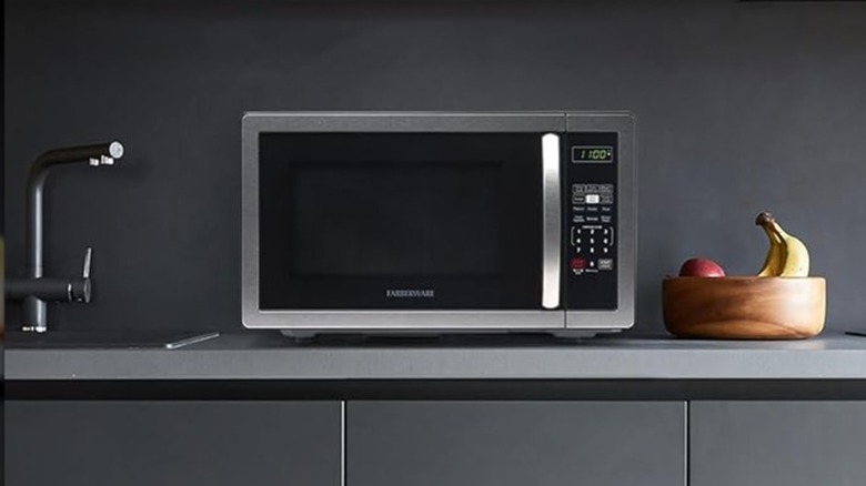 Farberware microwave sitting on a kitchen countertop next to a sink and a bowl of fruit