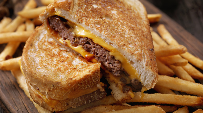 A grilled cheese with a ground beef patty inside, surrounded by french fries